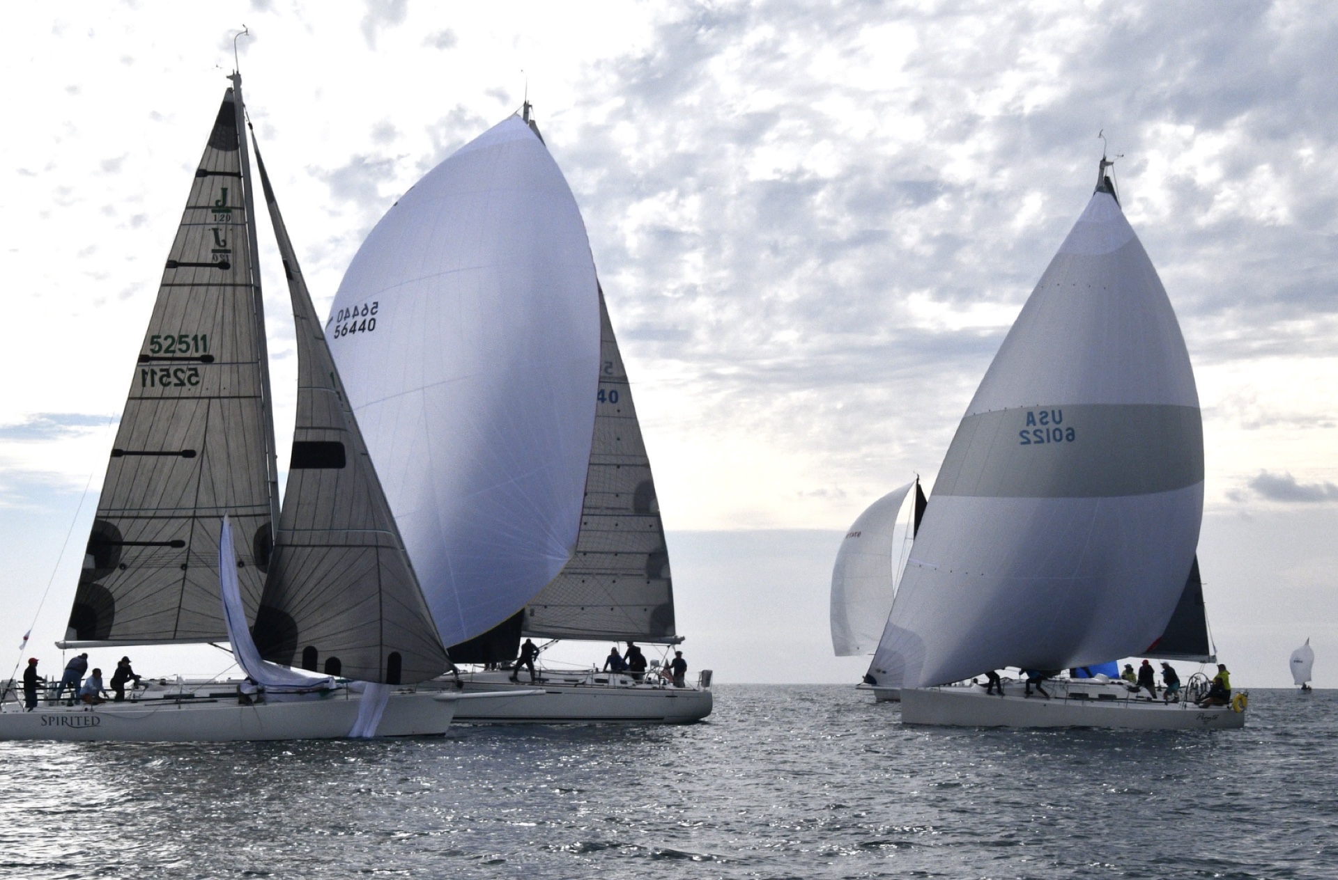 Sailboats under billowing white spinnakers gliding across the open ocean under dramatic clouds